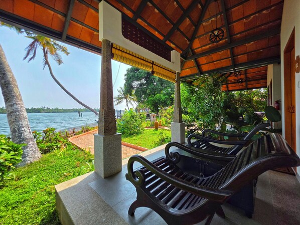 A covered outdoor seating area with a view of the sea, stone pillars, and a tiled floor.