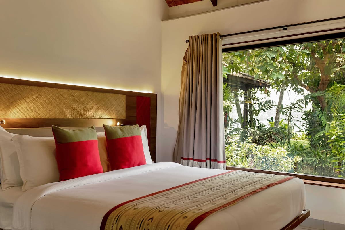 Ein Hotelzimmer mit einem großen Bett, einem Kopfteil mit strukturierter Gestaltung und Blick auf Grünflächen.