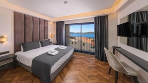 A hotel room with a bed, a desk, a chair, a TV, and a balcony with a view of the sea. - PİER HOUSE KAŞ (Kas)