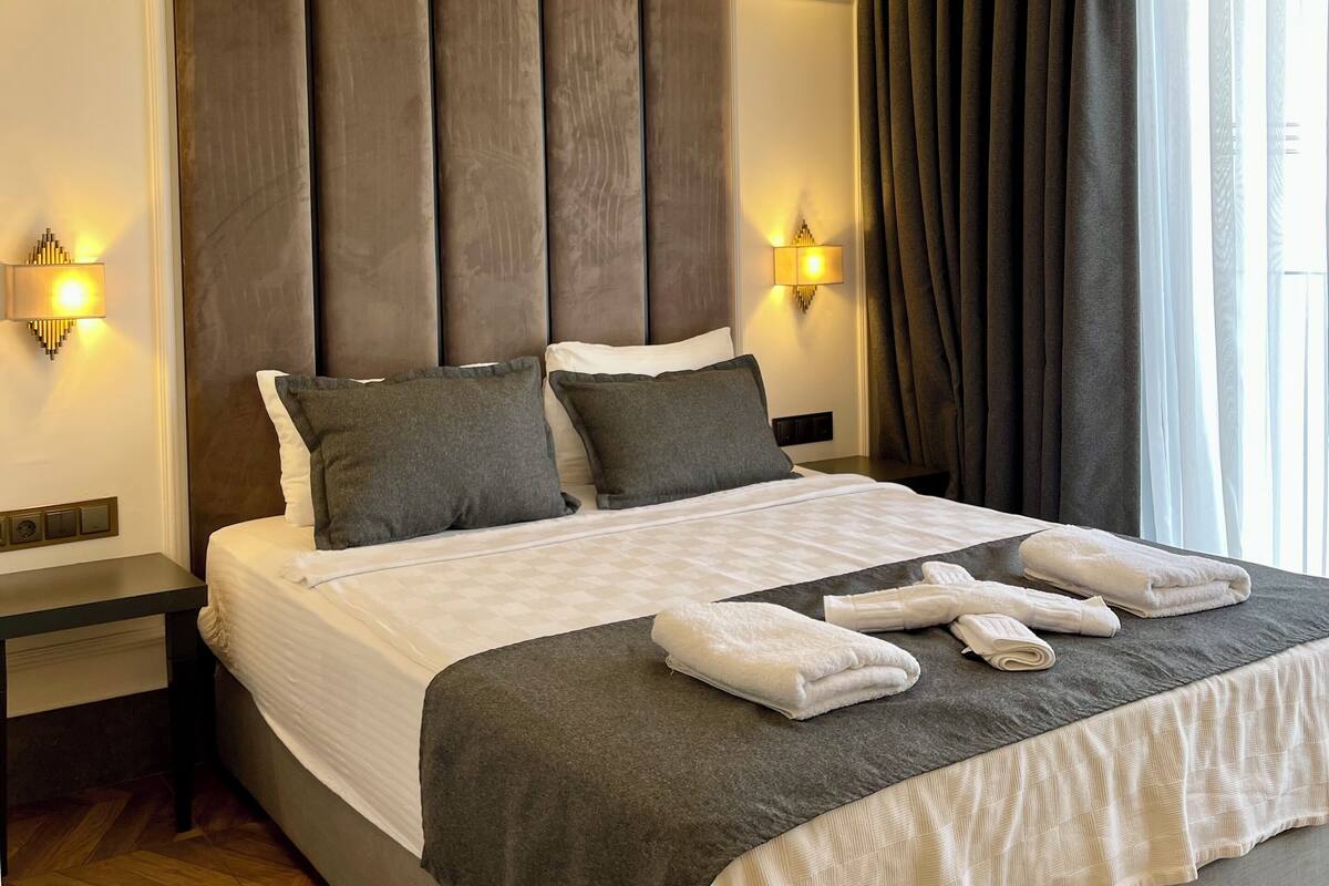 A modern hotel room with a large bed, grey bedding, and a wooden floor.