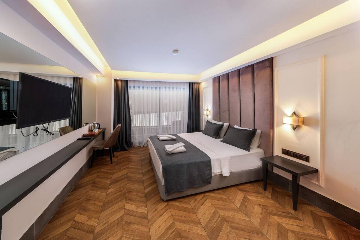 A hotel room with a bed, bedside table, desk with chair, and a TV mounted on the wall.
