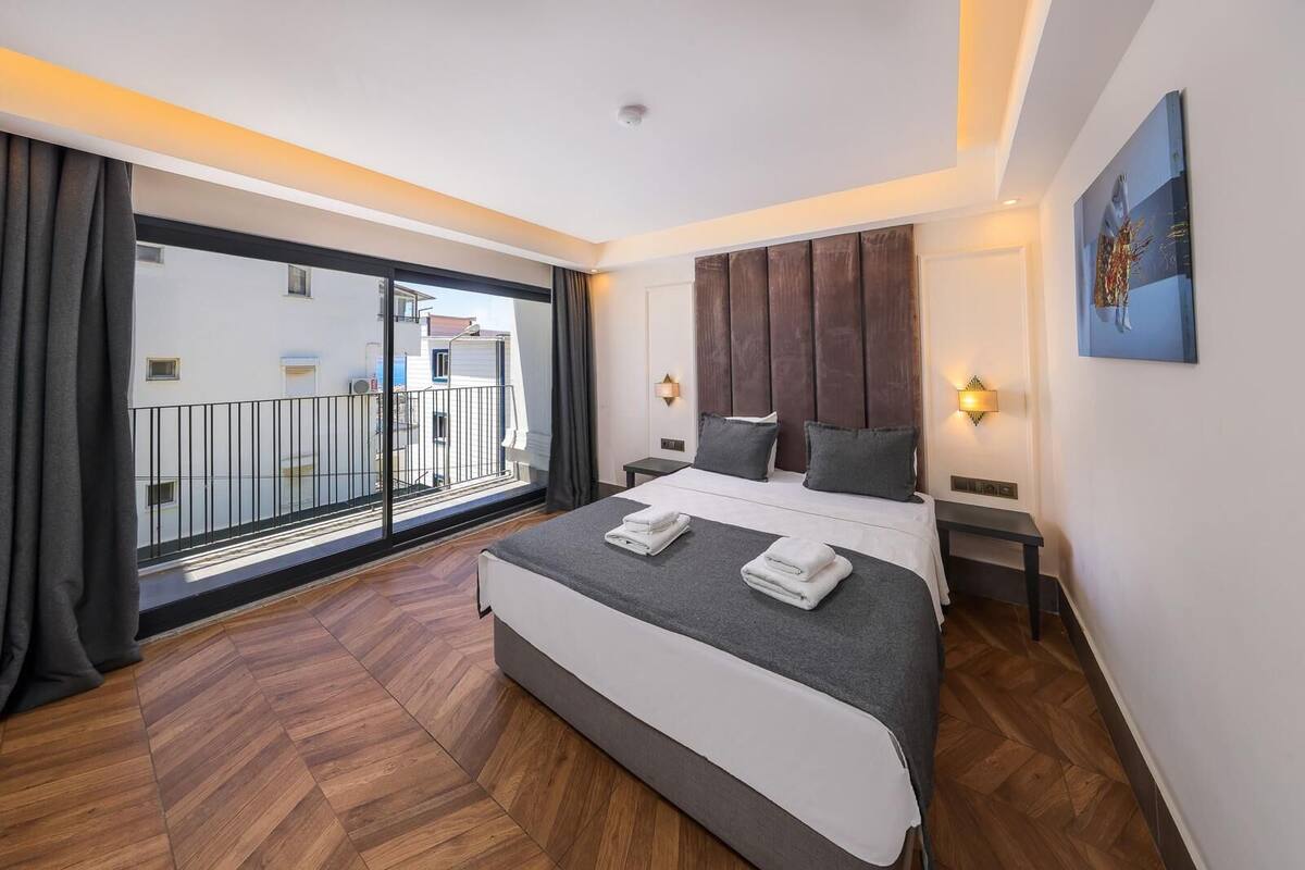 A modern hotel room with a large bed, a balcony with a view, and a painting on the wall.