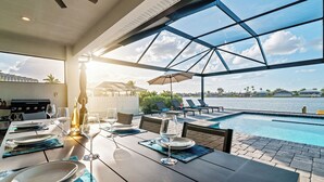 A dining area with a pool view, outdoor seating, and a grill. - Intervillas Florida - Villa Majadama (Cape Coral)