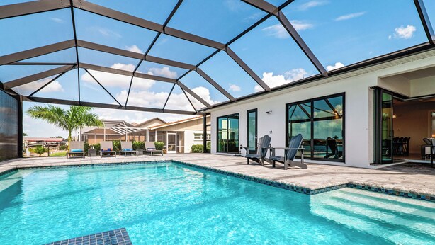 A swimming pool with a glass ceiling, lounge chairs, and a view of a building with large windows. - Intervillas Florida - Villa Majadama (Cape Coral)