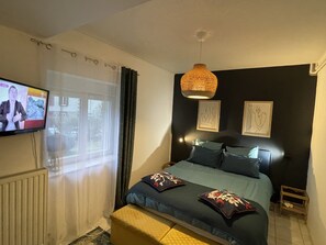 A bedroom with a bed, a television, a window with curtains, and artwork on the wall.