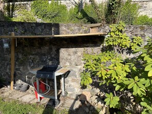 A stone wall with a wooden shelf, a barbecue grill, and a small birdhouse.