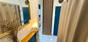 A hallway with a mirror, a plant, a door, and a light fixture.