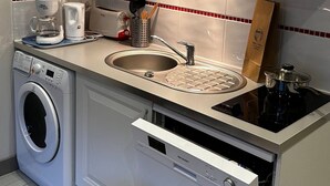 A compact kitchen with a microwave, coffee maker, sink, and a built-in washing machine.