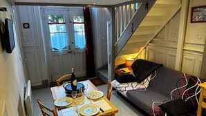 A dining area with a table set for two, a sofa, and a staircase leading to another level.