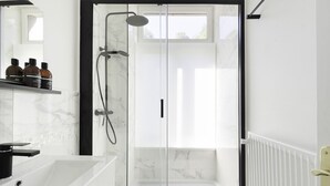 A modern bathroom with a glass-enclosed shower, a white marble sink, and a shelf with toiletries.