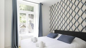A neatly made bed with white linens and two pillows, a window with curtains, and a geometric patterned wall.