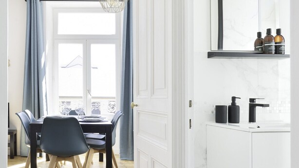 A modern kitchen with white cabinetry, a black countertop, and a window with blue curtains.