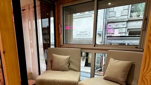A modern interior with two beige sofas, wooden flooring, and a view of the street outside. - Le Refuge des Skieurs (Mont-Dore)
