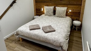 A bedroom with a wooden headboard, a bed with patterned bedding, a small stool, and a knife on the wall. - Le Refuge des Skieurs (Mont-Dore)