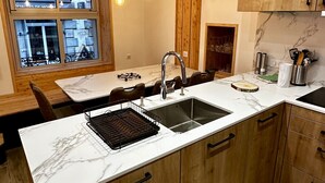 A modern kitchen with wooden cabinets, a marble countertop, a built-in sink, and pendant lighting. - Le Refuge des Skieurs (Mont-Dore)