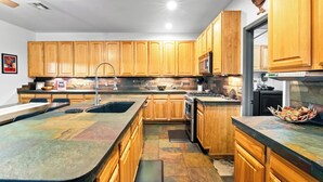 A kitchen with wooden cabinets, a granite countertop, a sink, a stove, and a microwave. - Serene desert escape w/ stunning mountain views & heated pool/spa- pet friendly! (Tucson)