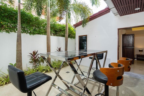 A modern outdoor seating area with a glass-top table and black and wooden chairs. - Tropical 3BR Pool Villa Amaya in Kamala (Kamala)