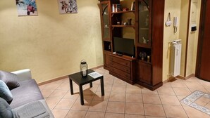 A living room with a sofa, a coffee table, a wooden cabinet with glass doors, and two wall-mounted pictures. - Two steps from the heart of Rome. (Roma)