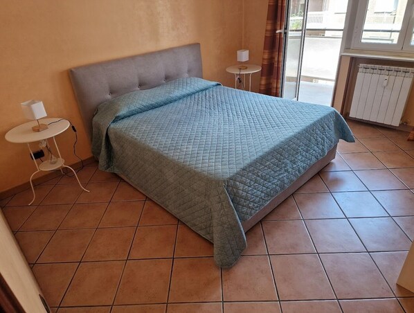 Ein Schlafzimmer mit einem Bett, zwei Nachttischen, einem Heizkörper und einem Fenster mit Vorhängen.