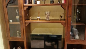 A wooden entertainment center with a flat-screen TV, glass-fronted shelves with books and decorative items, and a cabinet with drawers. - Two steps from the heart of Rome. (Roma)