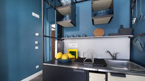 A modern kitchen with a black countertop, a sink, and a bowl of lemons. There are shelves above the counter holding plates and cups. - Design Flat (Piano di Sorrento)