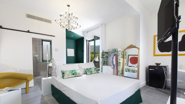 A modern bedroom with a large bed, a yellow chair, a wardrobe, and a mirror. - Design Flat (Piano di Sorrento)