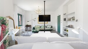 A modern bedroom with a large bed, a TV mounted on the wall, a chandelier, and a green sofa in the background. - Design Flat (Piano di Sorrento)