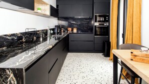 A modern kitchen with dark cabinetry, a marble countertop, and a speckled floor. - La Maison des Dunes - Plage à Pied (Cléder)