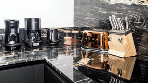 A kitchen with a black countertop, a coffee maker, a toaster, and a knife block. - La Maison des Dunes - Plage à Pied (Cléder)