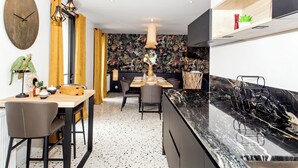 A modern kitchen with a marble countertop, a dining area with a wooden table and chairs, and a wall with a tropical wallpaper. - La Maison des Dunes - Plage à Pied (Cléder)