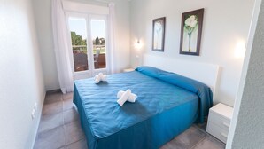 A bedroom with a large bed, a nightstand, a window with curtains, and two framed pictures on the wall. - Camelot in Oliva With 1 Bedrooms and 1 Bathrooms (Oliva)