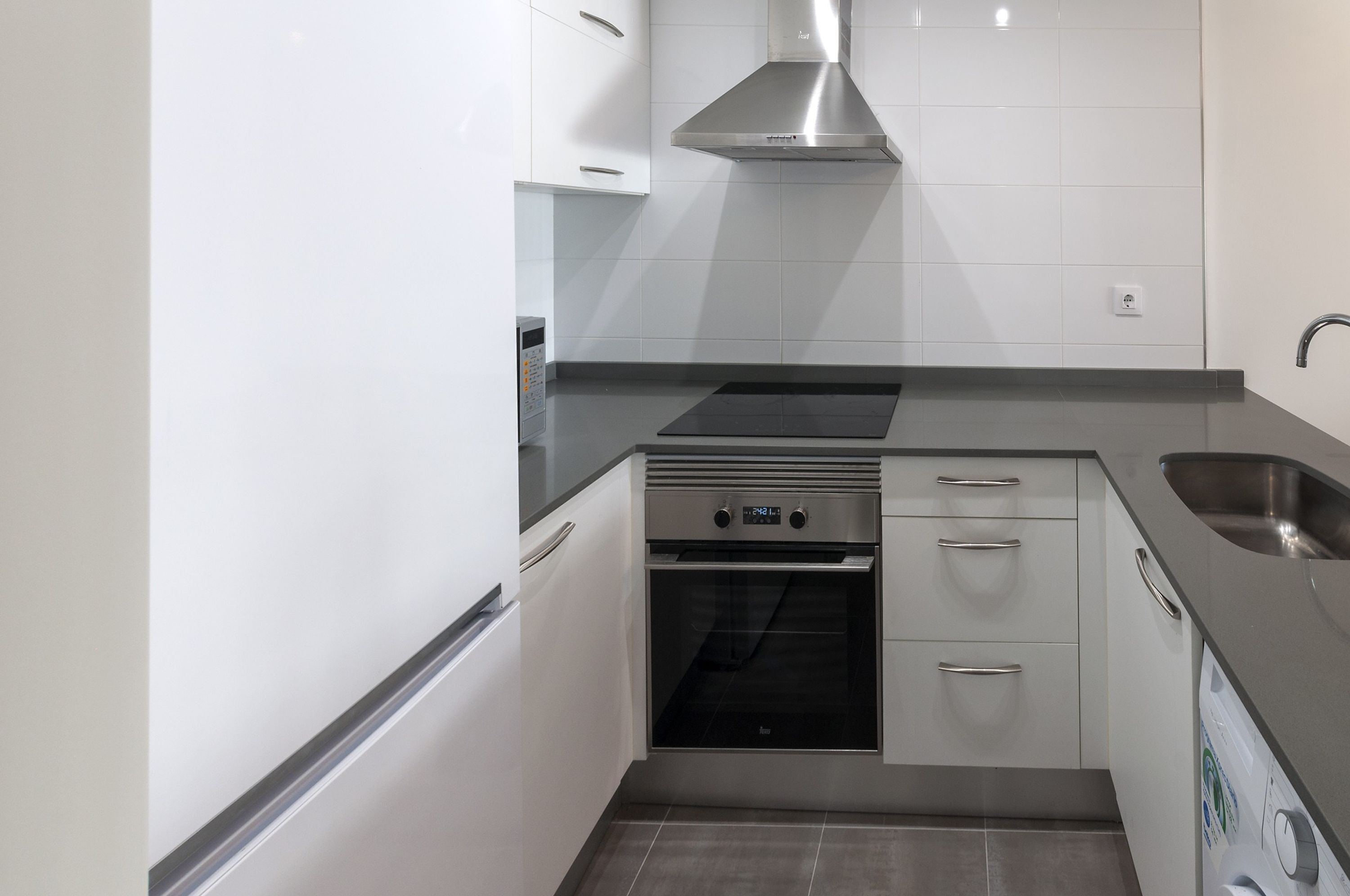 A compact kitchen with white cabinets, a stainless steel range hood, a built-in oven, and a dishwasher.