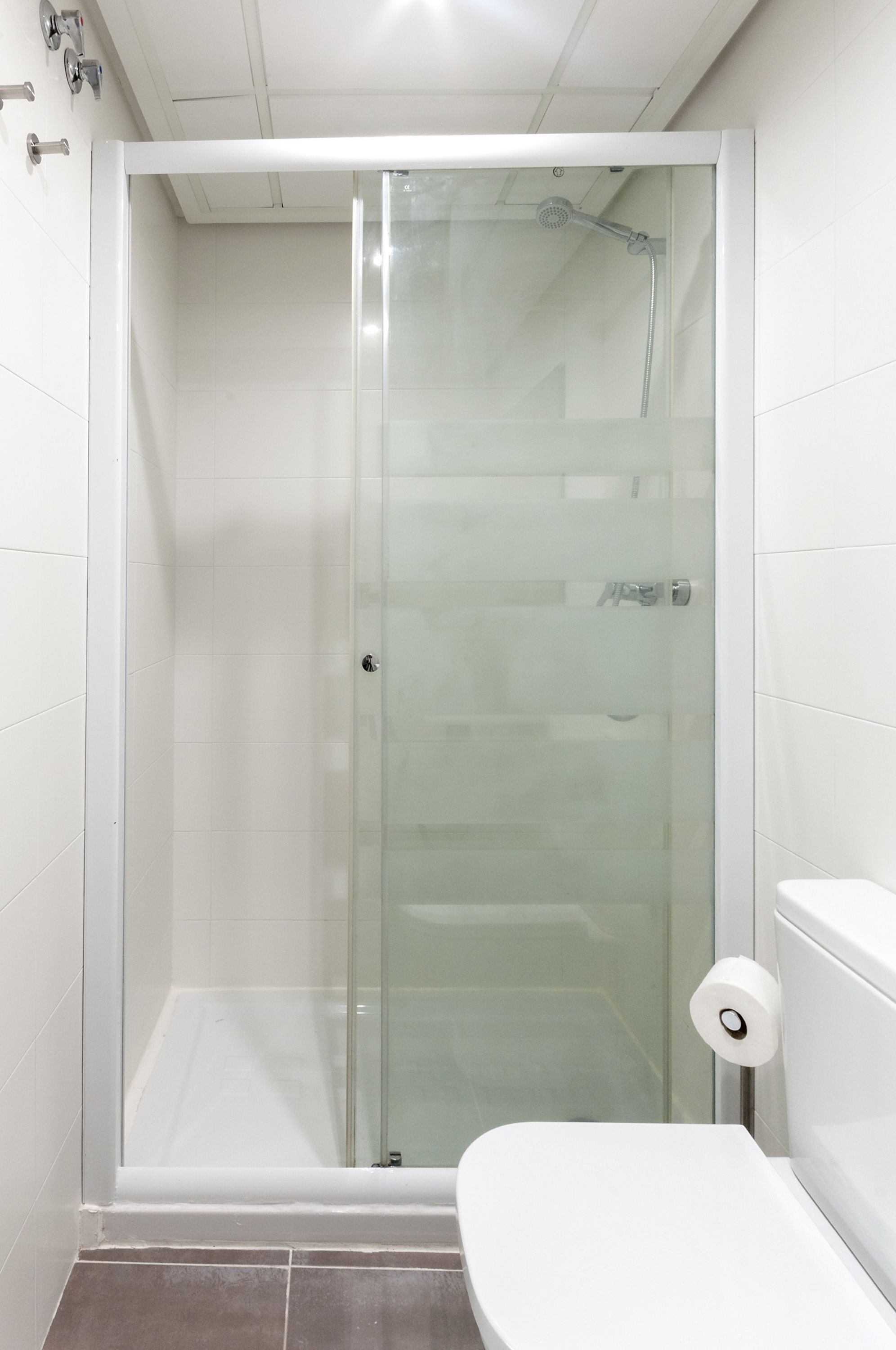 Une cabine de douche fermée par des parois en verre, avec des toilettes blanches et un distributeur de serviettes en papier.