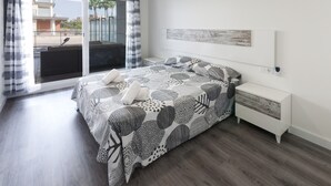 Een moderne slaapkamer met een groot bed, een witte nachtkastje en uitzicht buiten door een schuifdeur van glas.