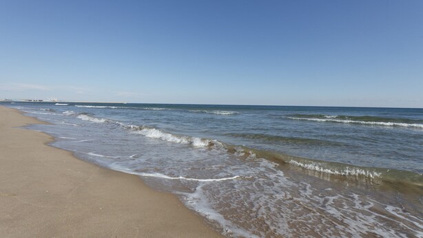 Een strand met heldere lucht en rustige golven.