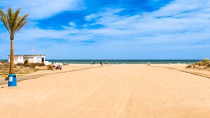 A sandy beach with a palm tree, a small building, and the ocean in the background. - Bambu in Grau i Platja (Gandia)