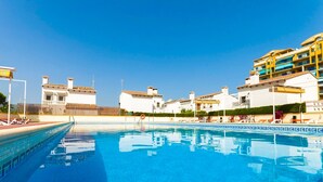 A swimming pool with clear blue water, surrounded by white buildings with balconies and a yellow building in the background. - Bambu in Grau i Platja (Gandia)