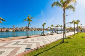 A waterfront promenade with palm trees, a patterned walkway, and a view of a historic building with a clock tower. - Bambu in Grau i Platja (Gandia)