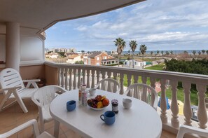 Un balcon avec une table dressée pour le petit-déjeuner, des chaises blanches et une vue sur la mer et les bâtiments.