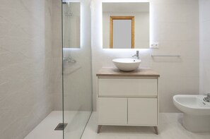 Une salle de bain moderne avec une douche à parois de verre, un meuble-lavabo en bois avec un lavabo blanc et un bidet.