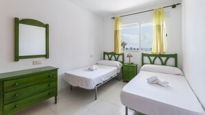 Een kamer met twee éénpersoonsbedden, een groene dressoir, een nachtkastje en een raam met gordijnen.