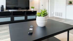 A black table with a remote control and a white pot with green plants.
