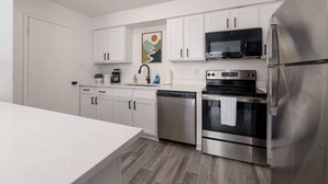A modern kitchen with white cabinets, stainless steel appliances, and a wooden floor.