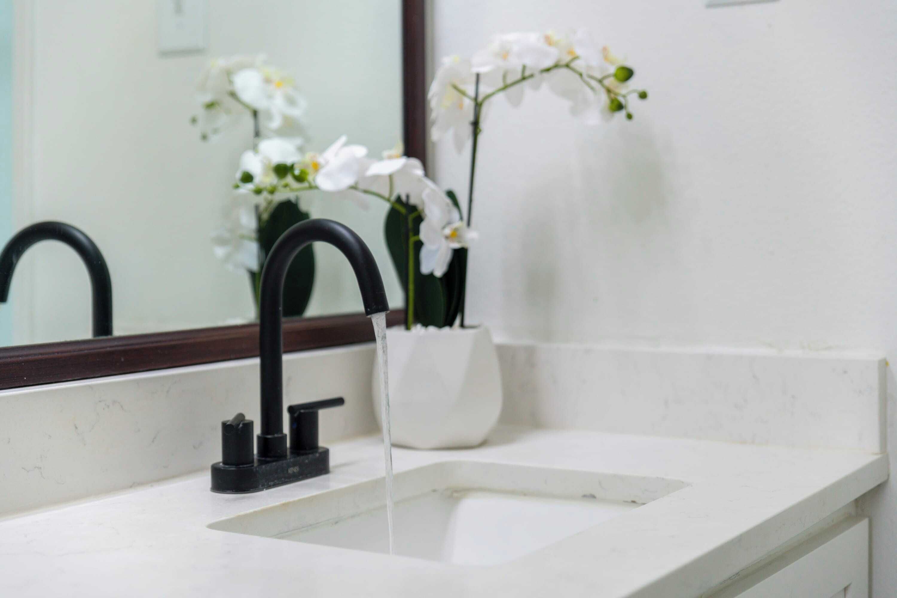 A bathroom with a white sink, black faucet, and a white vase with white flowers.