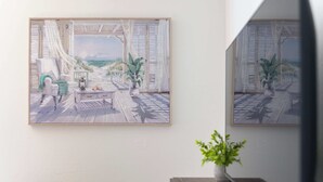 A room with a large window overlooking a deck with a view of the ocean. There is a chair and a small table with a plant on it. - Modern Poolside Apartment Near Gruene (New Braunfels)
