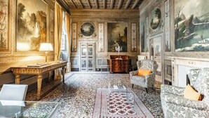 A grand room with ornate ceiling, classical paintings, and plush seating.