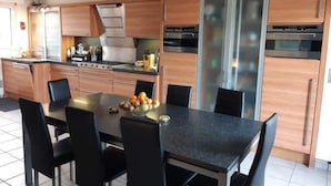 A modern kitchen with wooden cabinets, a black countertop, and a dining table with chairs. - Maison Presqu'ile de Gâvres (Gâvres)