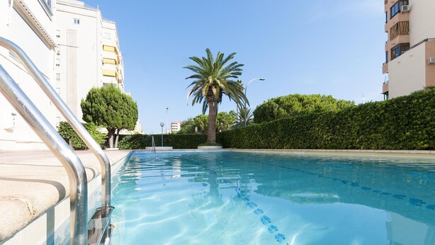 A swimming pool with metal railings, surrounded by greenery and buildings. - Acapulco Iv in Grau i Platja (Gandia)