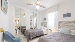 A bedroom with two beds, a ceiling fan, a large mirror, and a view of the beach. - Benalmar Playa in Benalmadena (Benalmádena)