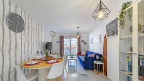 A modern living room with a sofa, a dining area with a table set for two, and a bookshelf filled with books. - Benalmar Playa in Benalmadena (Benalmádena)